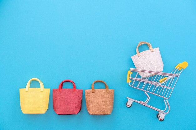 Photo abstract design element, annual sale, shopping season concept, mini yellow cart with colorful paper bag on pastel blue background, top view, flat lay