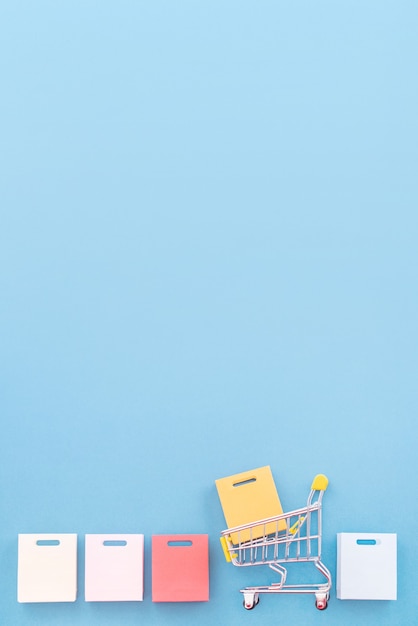 Photo abstract design element, annual sale, shopping season concept, mini yellow cart with colorful paper bag on pastel blue background, top view, flat lay