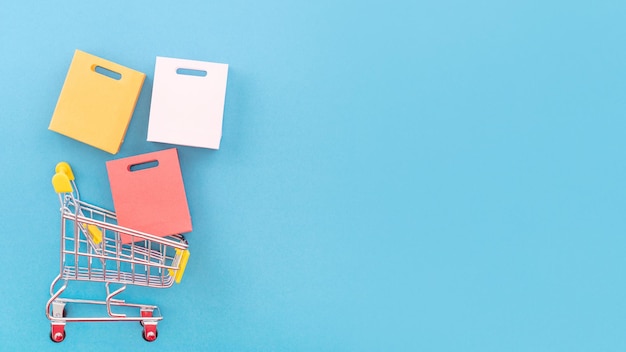 Photo abstract design element annual sale shopping season concept mini yellow cart with colorful paper bag on pastel blue background top view flat lay