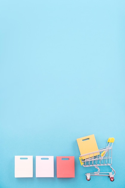 Photo abstract design element concept of annual sale shopping season mini yellow cart with paper bag isolated on pastel blue background top view flat lay