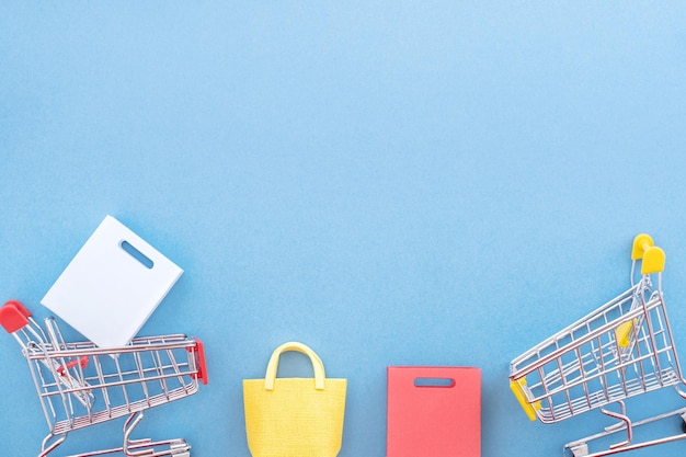 Photo abstract design element concept of annual sale shopping season mini yellow cart with paper bag isolated on pastel blue background top view flat lay