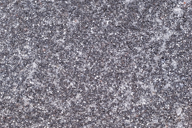 Abstract texture of the frozen asphalt of dark color with white snow grains for a natural background