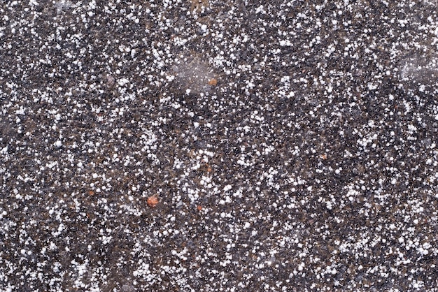 Abstract texture of the frozen asphalt of dark color with white snow grains for a natural background