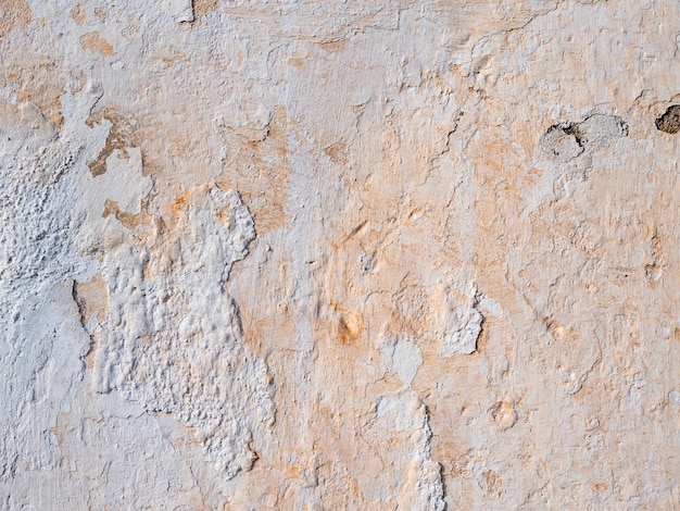 Abstract texture of an old beige weathered wall with cracked and peeling plaster