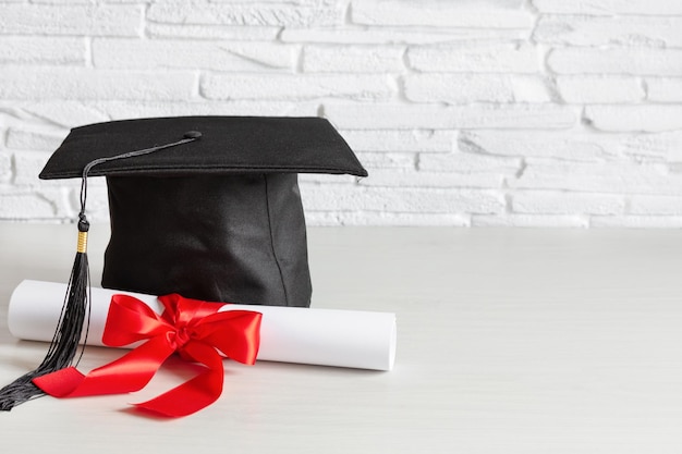 Academic cap and graduation diploma scroll and tied with red ribbon