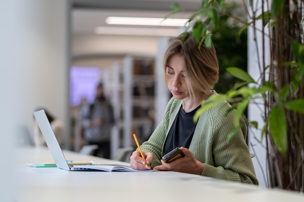 Academic career female university professor taking notes in day planner while sitting in library