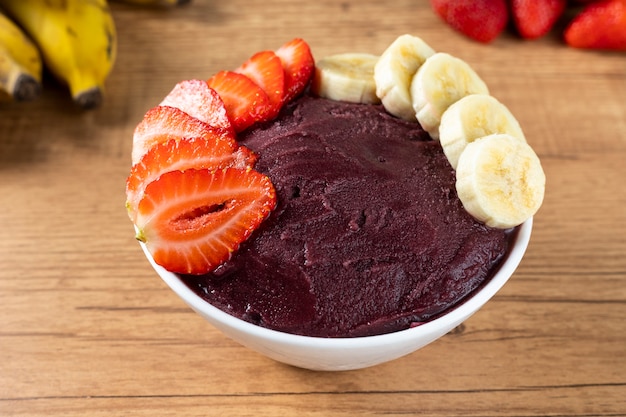 Acai, Brazilian frozen Acai berry ice cream bowl with strawberries and bananas. with fruits on wooden table. Summer menu front view