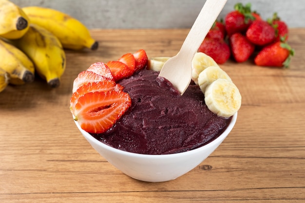 Acai, Brazilian frozen Acai berry ice cream bowl with strawberries and bananas. with fruits on wooden table. Summer menu front view