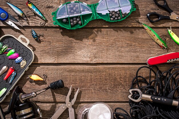 Accessories for fishing on the background of wood. Reel, fishing line, float, net hooks, lures for fishing. Top view. Still life. Copy space