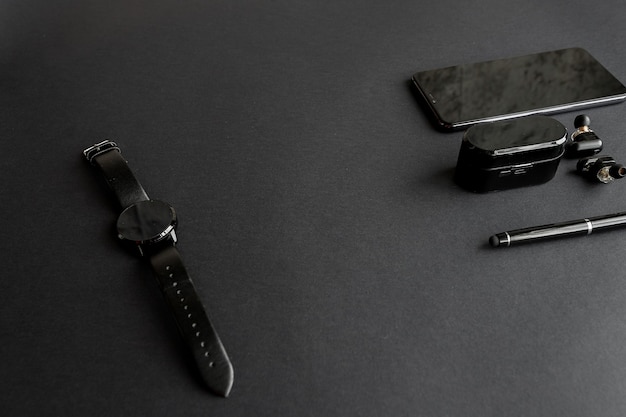 Accessories for men's beauty on a monochromatic background. black pen, black smart watch, smartphone and wireless headphones on dark background. View from above. Minimalist black trend 2020.