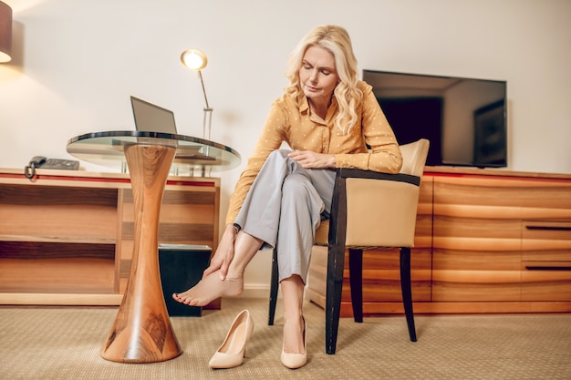 Aching feet. Blonde woman looking tired and taking off shoes