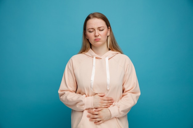 Aching young blonde woman keeping hands on belly with closed eyes 