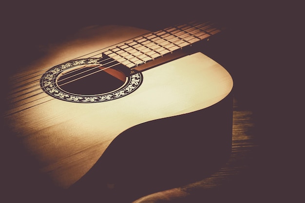 Acoustic guitar lying on a wooden table lit by a beam of light