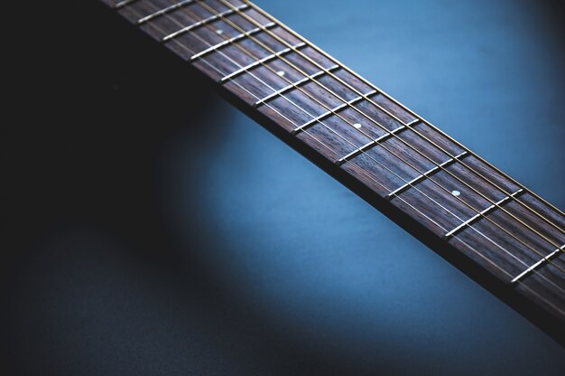 Acoustic guitar, music instrument resting against a dark blackv wall with copy space, Close-up of wooden classic guitar