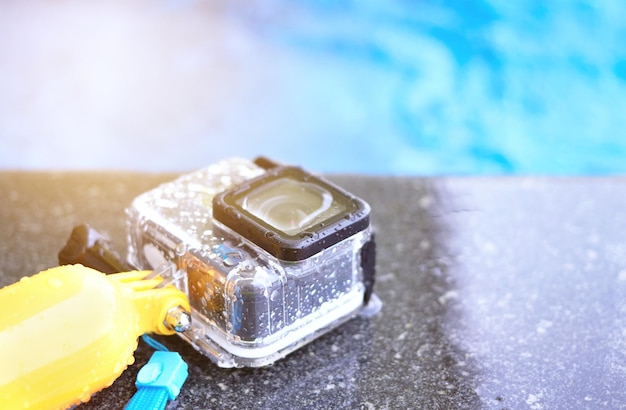 Action camera in waterproof case and floater grip on poolside and blur swimming pool