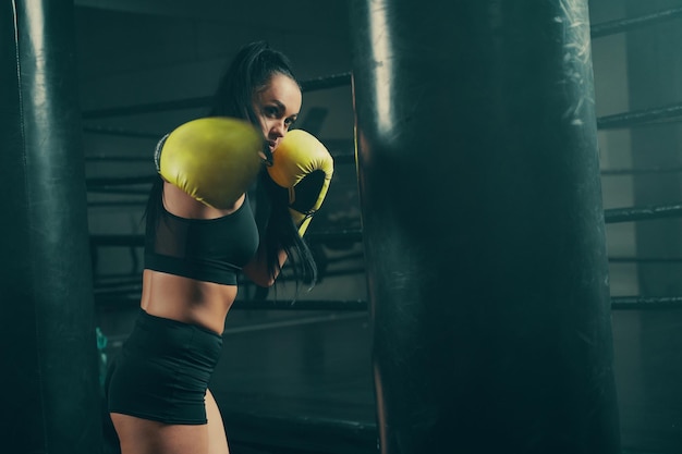 Action shot of young athletic woman training with punching bag wearing yellow boxing gloves