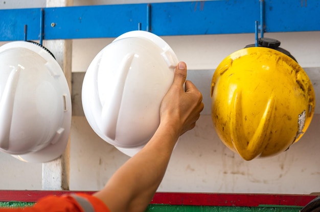 Action of a worker is taking a safety helmet or hardhat from the hanging rack