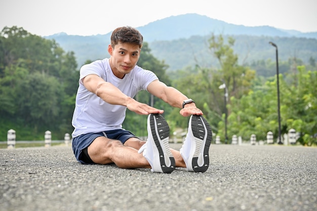 Active Asian athletic man in sportswear and running shoes stretching his legs on the road