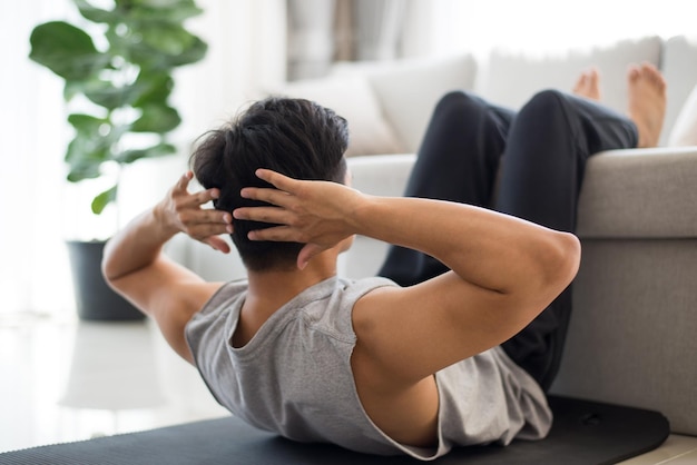 Active asian man wearing gray sport wear doing abs training and crunches in living room at home During the quarantine due to the spread of the coronavirus