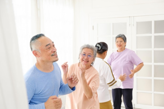 Active Asian senior group mix with man and woman exercise by dancing together at home with relaxing smiling and laughing Indoor activity for mature seniors and retirement people Focus on senior man