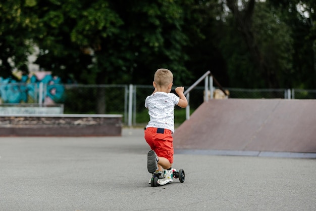 Active boy riding a scooter in the summer skate park