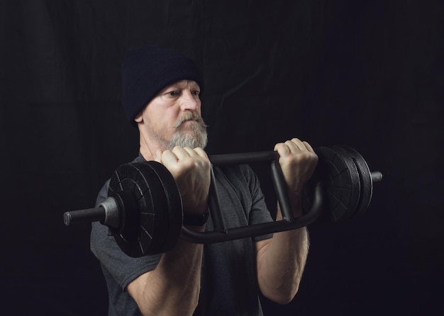 Active elderly man with a beard trains biceps with a barbell