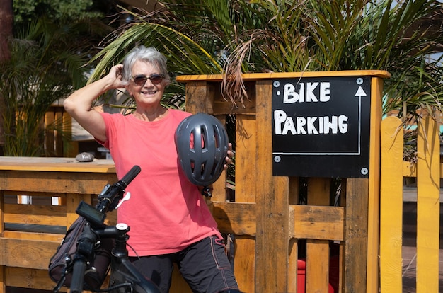 Active elderly woman on excursion with her bicycle wearing protective helmet stops at aperitif bar with parking area for cyclists