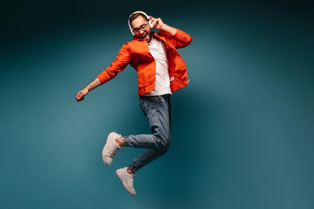 Active guy in headphones jumps on blue background