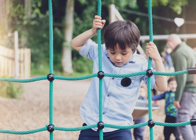 Active kid climbing rope in the playground,, Child enjoying activity in a climbing adventure park on summer sunny day, Cute little boy having fun on a playground outdoors.