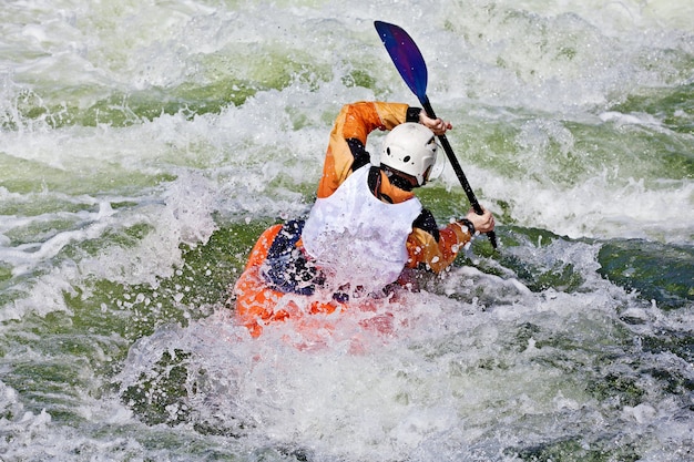 An active male kayaker rolling and surfing in rough water