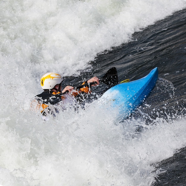 An active male kayaker rolling and surfing in rough water