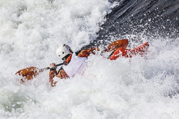 An active male kayaker rolling and surfing in rough water