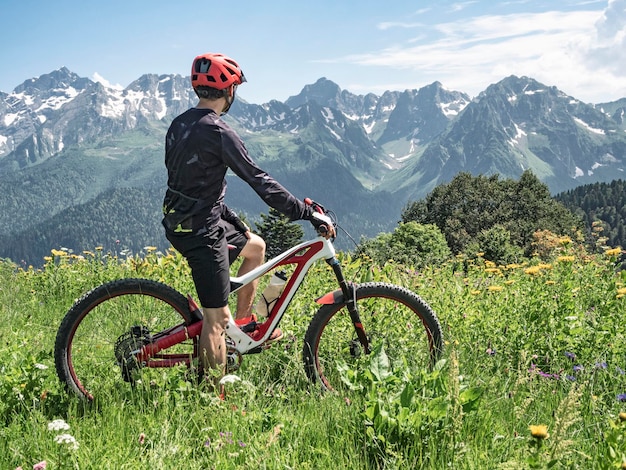 Active man standing with bicycle on alpine meadows at panoramic mountains background