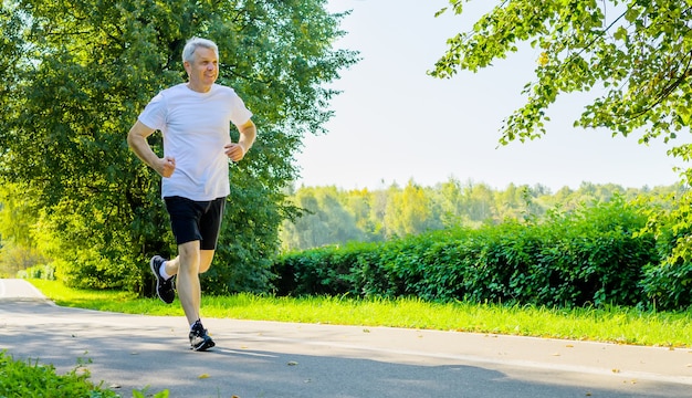 Active mature man running in park during morning workout at springtime.