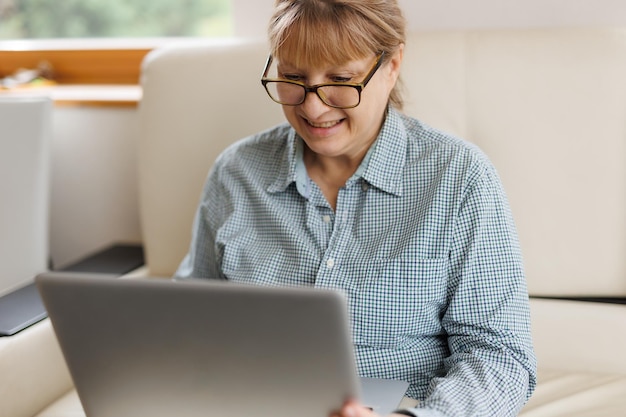 Active mature woman using a laptop for remote work from the home office Video conference video meeting Senior teacher leads webinar