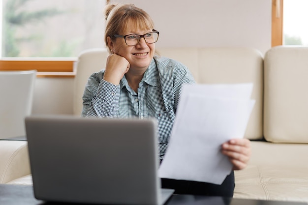 Active mature woman using a laptop for remote work from the home office Video conference video meeting Senior teacher leads webinar