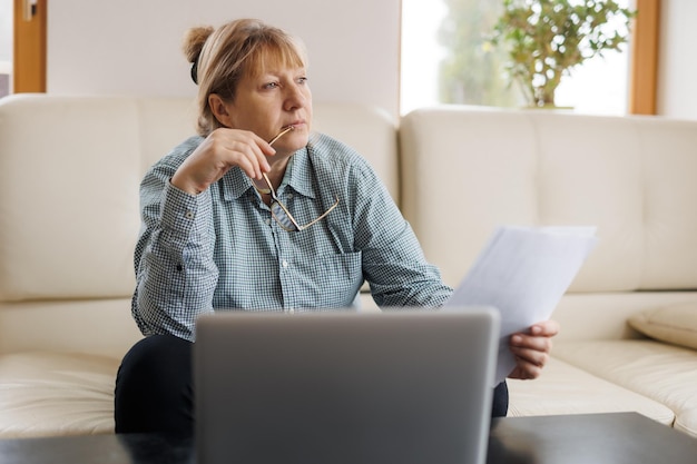 Active mature woman using a laptop for remote work from the home office Video conference video meeting Senior teacher leads webinar