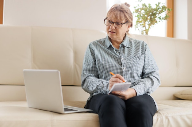 Active mature woman using a laptop for remote work from the home office Video conference video meeting Senior teacher leads webinar