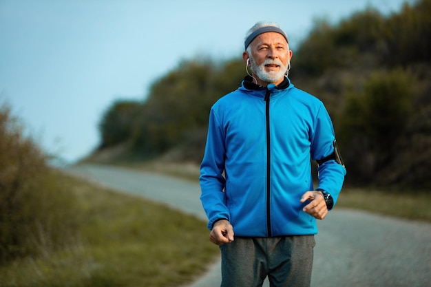 Active senior athlete feeling motivated while running in nature and listening music on earphones Copy space