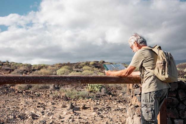 Active senior bearded man in outdoor excursion consulting his map wearing backpack Elderly whitehaired pensioner enjoying freedom and healthy lifestyle