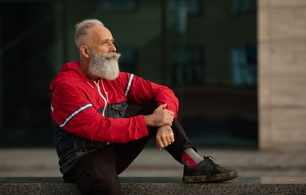 Active senior man walking in the city. Portrait of senior man with a beard while standing outside.