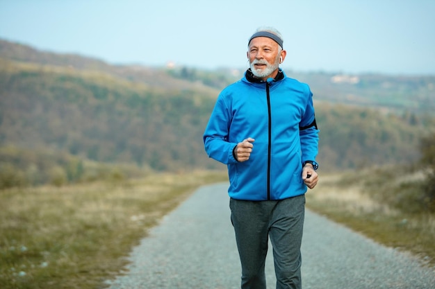 Active senior sportsman jogging in nature while listening music on earphones Copy space