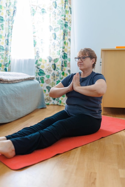 Active senior woman doing abs exercises on yoga mat at home and smiling at camera