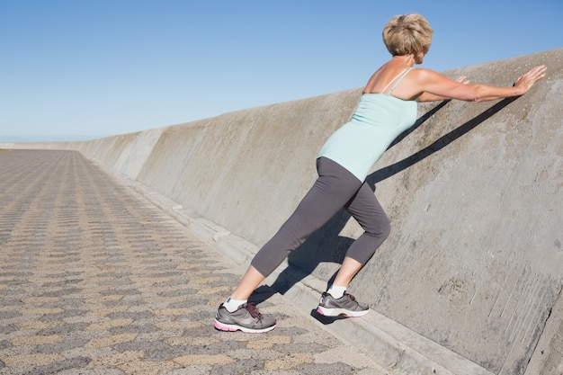 Active senior woman stretching on the pier