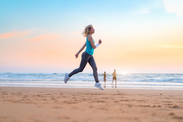 Active sporty woman run along ocean surf by water pool to keep fit and health Sunset sand beach background with sun Woman fitness jogging workout and sport activity