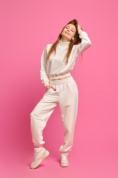 Active woman in white fleece sweatshirt and sweatpants posing over bright pink studio background