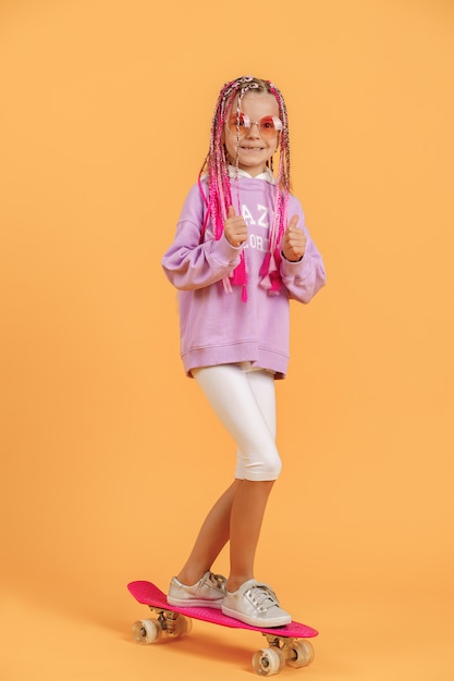 Active young girl in pink shirt and white shorts standing on skateboard