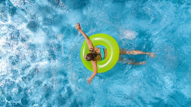 Active young girl in swimming pool aerial top view from above child swims on inflatable ring