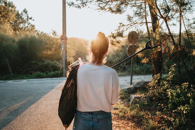 Activist young woman picking up trash with garbage tongs backwards to cameraForest background with