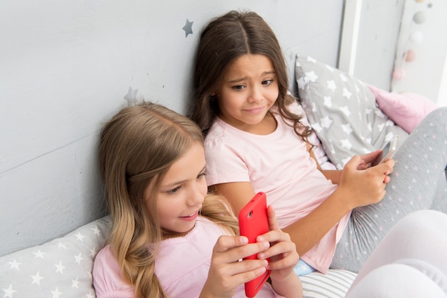 Activities for pajama party. Girls kids best friends or sisters wear pajama busy with smartphones. Children in pajama interact with smartphones. Technologies for kids generation. Pajama party ideas.